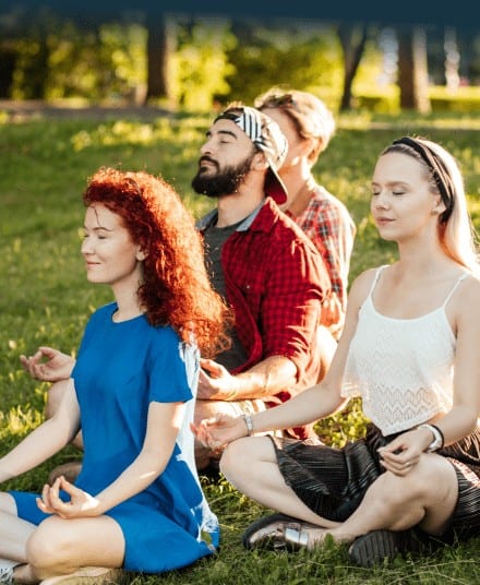 Group meditating outdoors in sunny park.